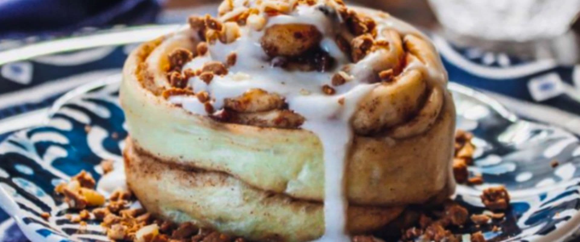 A frosted cinnamon roll topped with crumbled nuts, served on a decorative plate.