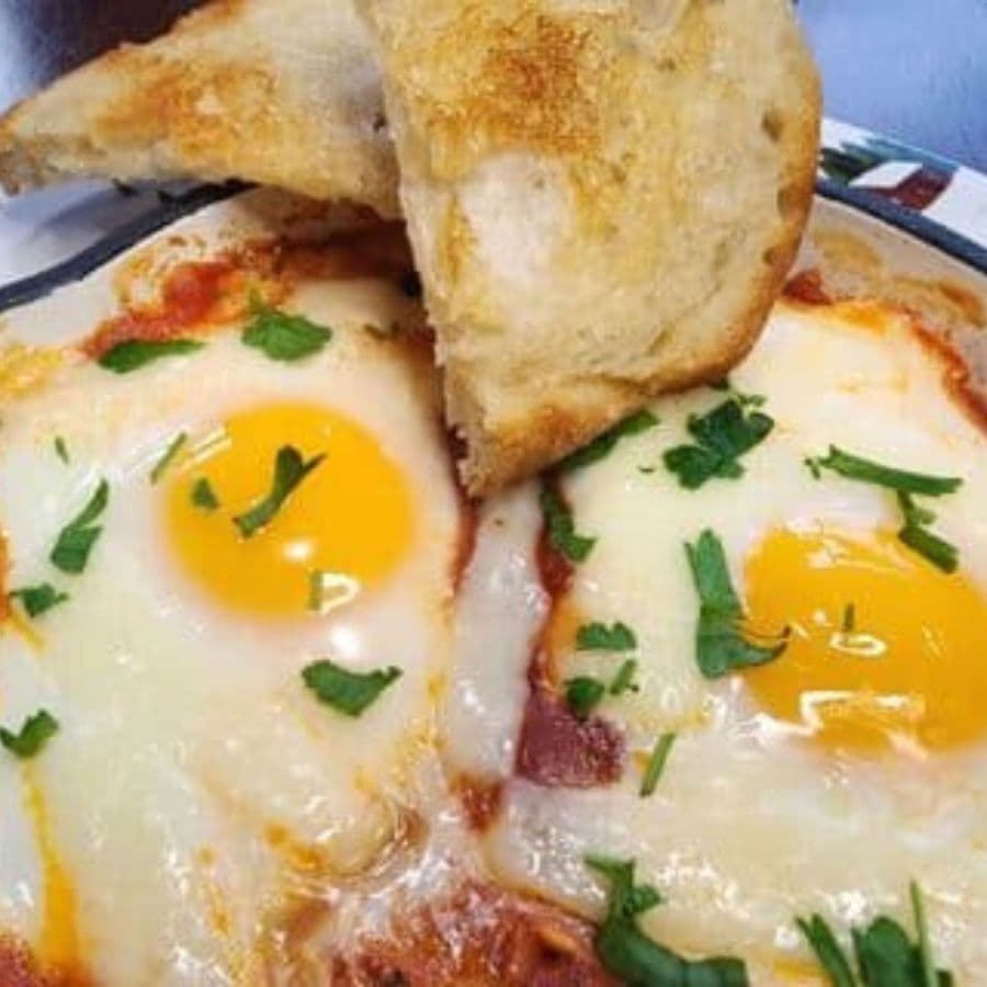 A plate of baked eggs topped with herbs and served with a slice of toasted bread.