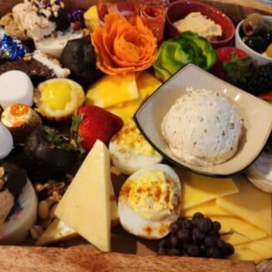 A colorful spread of various cheeses, fruits, and snacks arranged on a wooden platter.