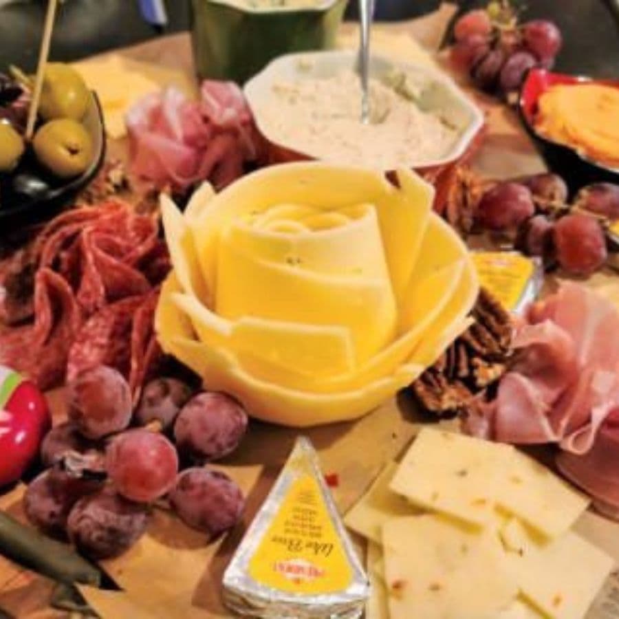 A decorative cheese platter featuring sliced meats, grapes, and various cheeses.
