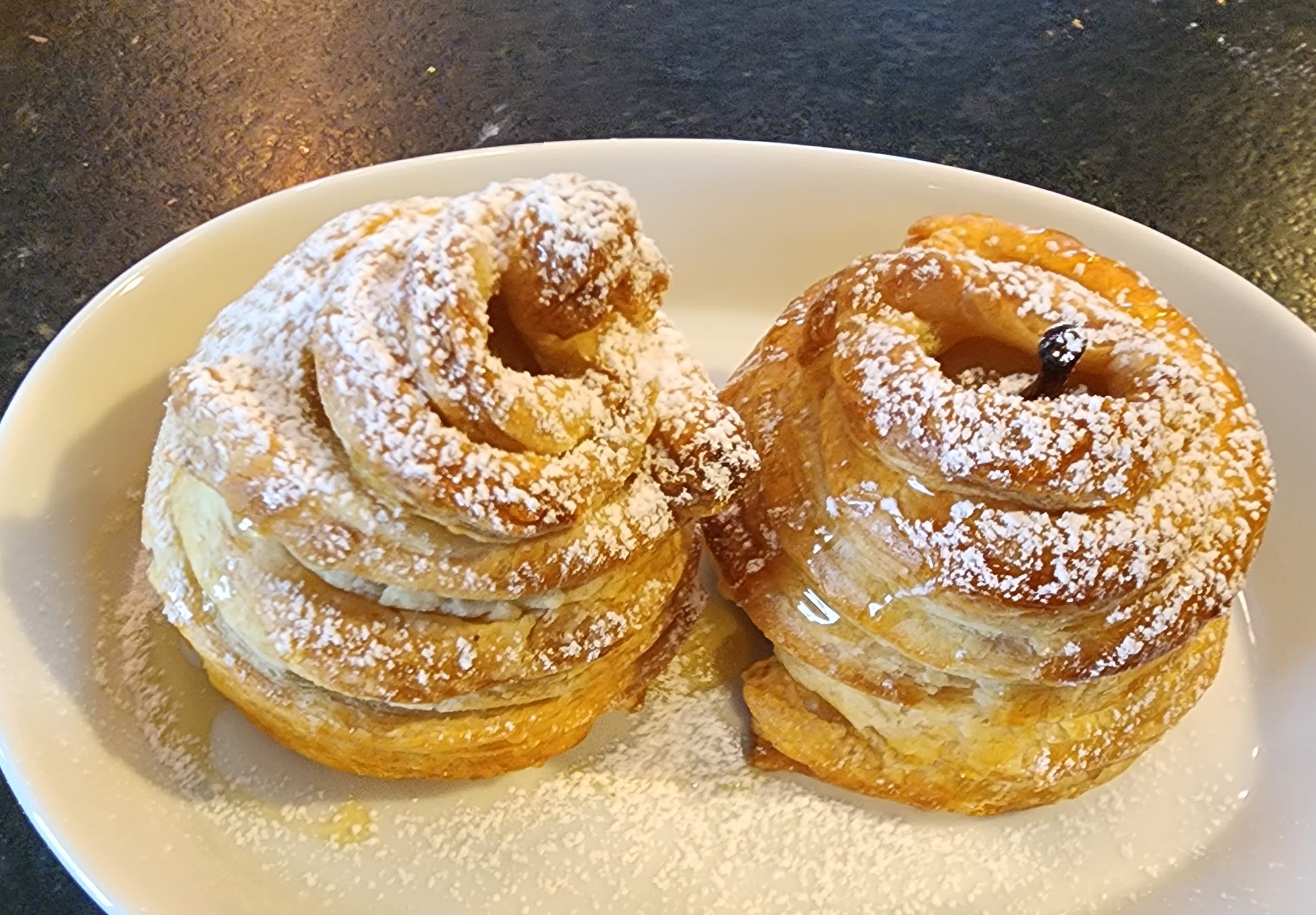 Two spiral pastries dusted with powdered sugar on a white plate.