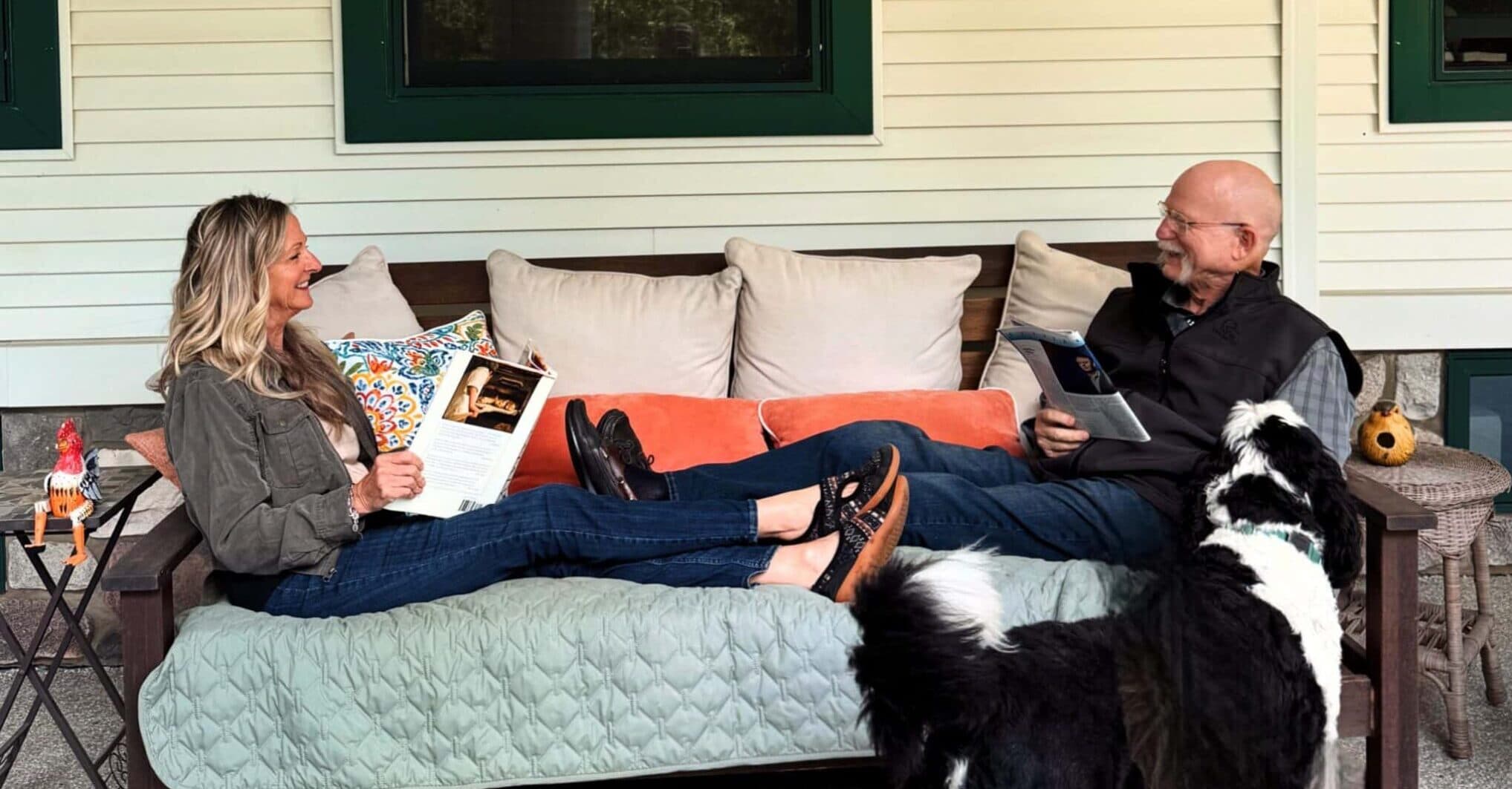 A woman and a man sit on a couch, enjoying books and an accompanying dog on a porch. A woman and a man sit on a couch, enjoying books and an accompanying dog on a porch.