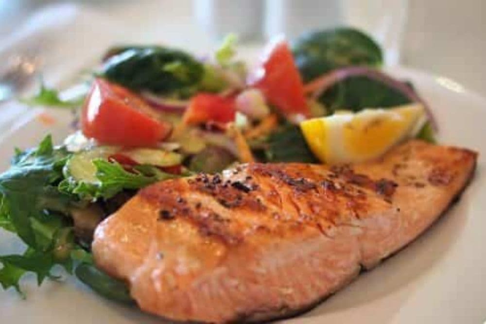 Grilled salmon fillet served with a mixed salad and lemon slices.