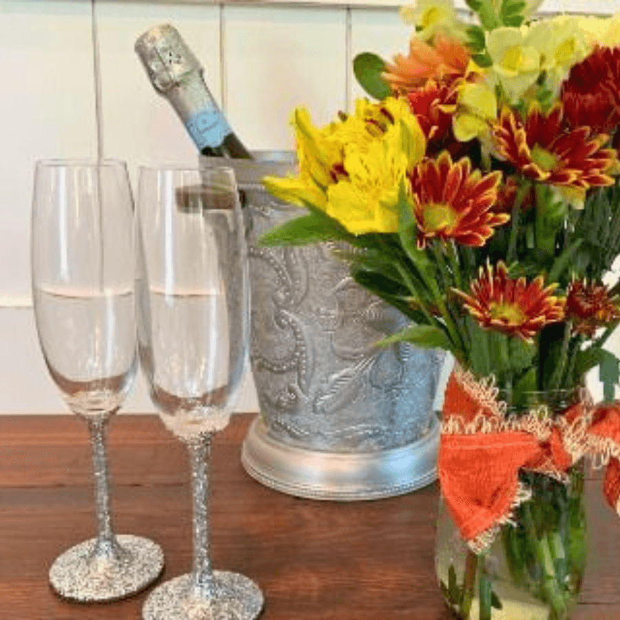 Two sparkling wine glasses beside a silver ice bucket and a colorful flower arrangement.