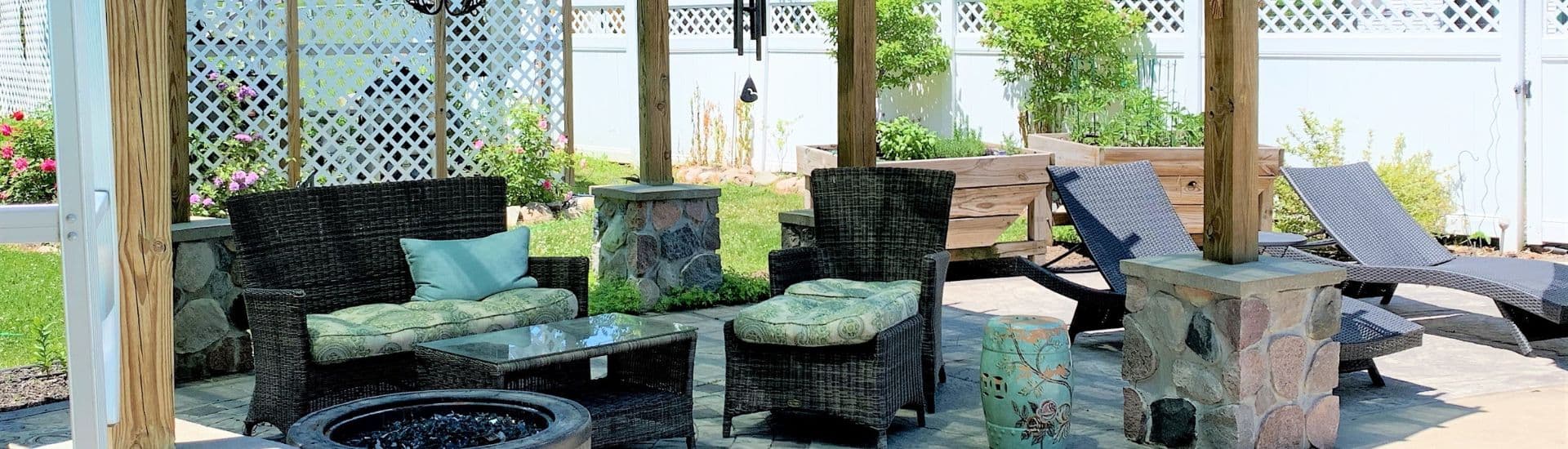 A cozy outdoor seating area with wicker chairs, a stone fire pit, and lounge chairs under a pergola.